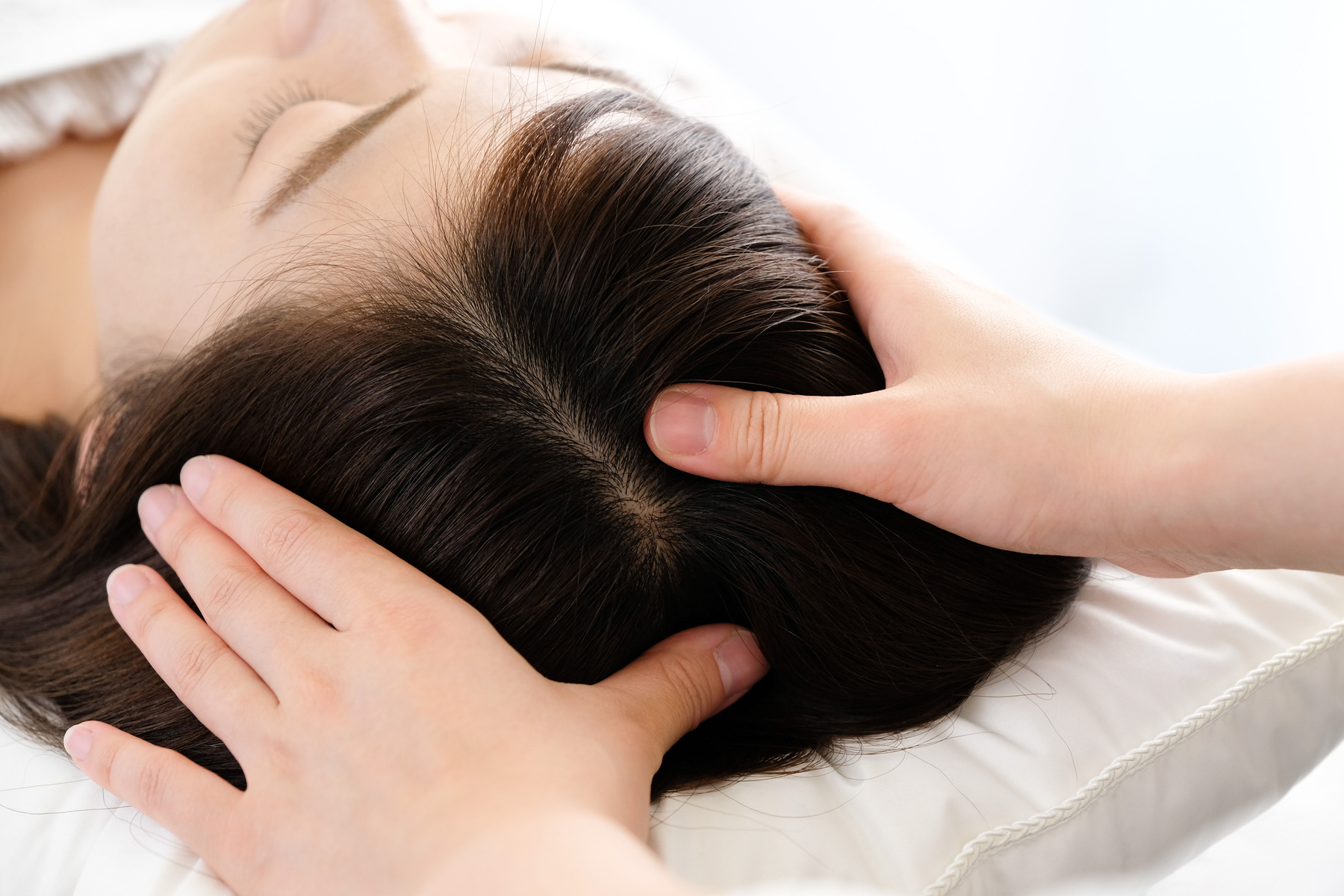 Woman receiving a scalp massage and the practitioner's hand